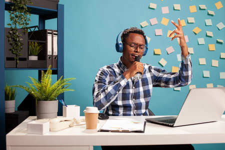Positive businessman listening to music and singing along at his modern workspace. Young male...
