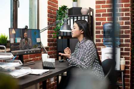 Asian entrepreneur discusses strategies with a client during virtual meeting in brick wall office....