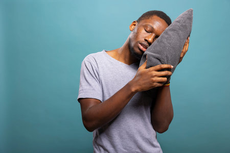 Sleepy african american man resting his head on a pillow, feeling exhausted and struggling to stay...