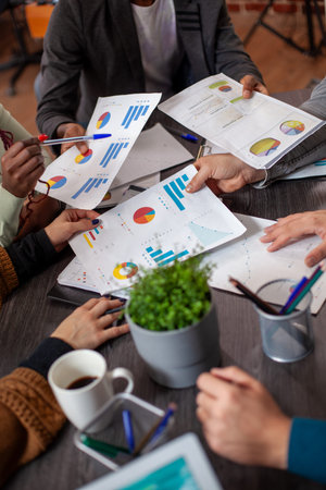 Group of people touching different documents placed on table with plant pot and coffee nearby....
