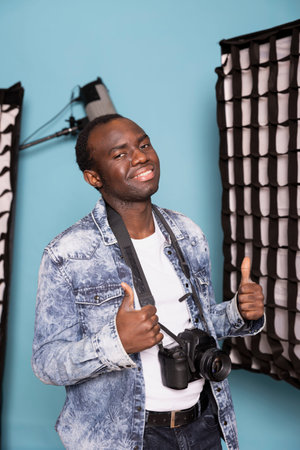 Happy male photographer showing two thumbs up after successful client photoshoot session in studio....