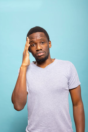 Portrait of an upset male adult experiencing a migraine, pressing his temple to relieve discomfort....