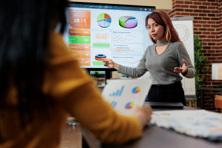 Asian manager discussing management statistics with entrepreneur woman during business meeting in...
