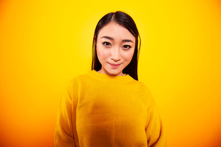 Beautiful asian woman in a yellow pullover sweater posing against a yellow background. Closeup...