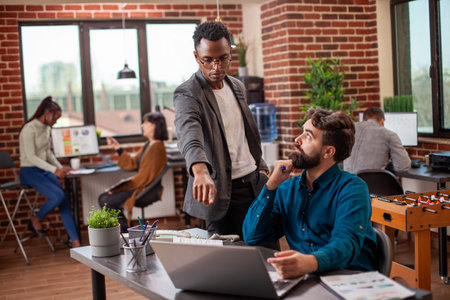 Male analyst points at laptop screen, explaining market analysis update to caucasian coworker....