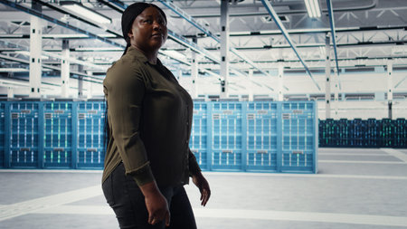 Data center admin conducts security audits to protect against cyber threats and vulnerabilities. Woman walking in server room, ensuring compliance with industry standards, camera Aの写真素材