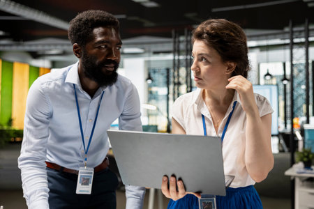 Businesswoman stands with male colleague, reviewing statistics and corporate data on laptop....