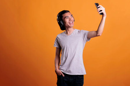 Smiling asian teenager taking photo on smartphone front camera. Young cheerful attractive man in...