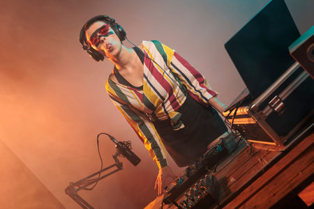 Flirty woman DJ acting silly with tongue out, fooling around in studio with lights. Playful funky...