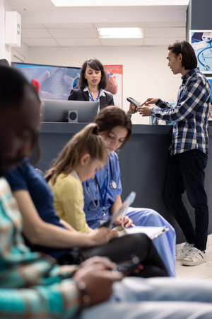 Caucasian female receptionist helps male patient complete payment at hospital front desk. Young...