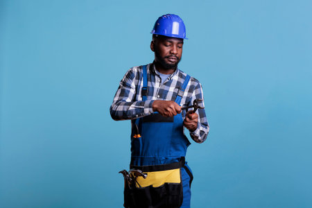 African american builder concentrating while using pliers against blue background. Studio portrait...