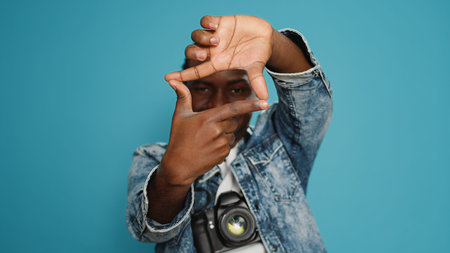 Male model doing frame shape sign with hands in front of studio camera, working as professional photographer with shooting equipment. Person with creativity going on adventure.の写真素材