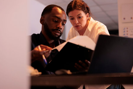 Project manager helping coworker checking report statistics, comparing data on laptop in office at...