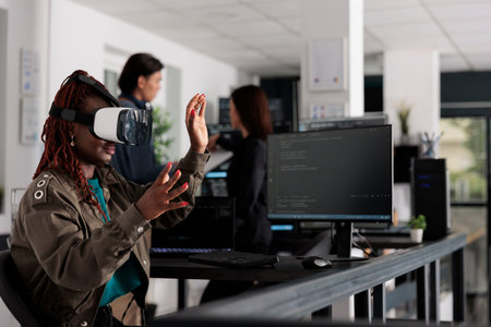 African american system engineer wearing virtual reality goggles working to develop security program...