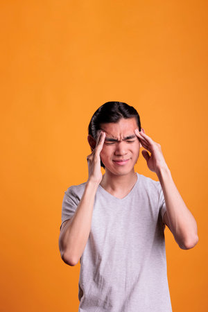 Young man suffering from migraine symptoms, touching temples with fingers. Exhausted asian teenager...