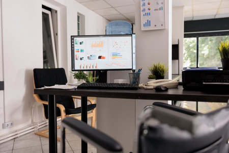 Close up view wheelchair in empty space with data and analysis statistics on tabletop computer monitor. Business workplace for corporate database, office wheelchair accessible.の写真素材