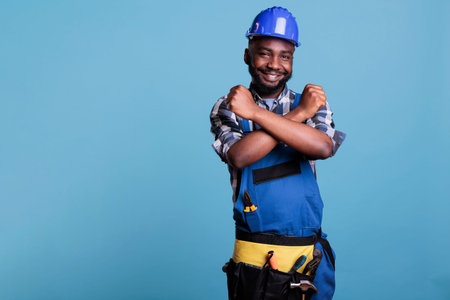Construction worker making a gesture of refusal with arms, standing on a blue background in a...