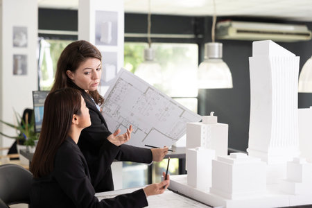 Caucasian manager explains project floor plans to coworker while examining white architectural...