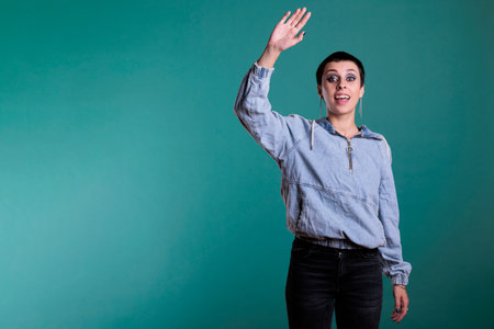 Confident attractive woman waving with palm at camera having fun in studio, smiling person being...