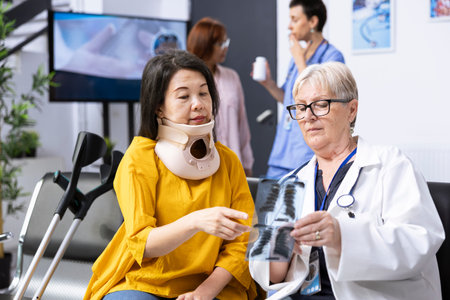 Person suffers from spine injury and is forced to wear cervical collar, receiving professional treatment at healthcare facility. Medic discussing vertebra healing strategies and providing advice.の写真素材