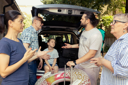 Open trunk and the baggage ready as large family group pack for holiday, grandparents and young parents with their little child prepare the car for road trip. Laughter and love under the sun.の写真素材