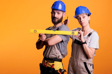 Construction workers holding screwdriver and water level in studio shot, using ruler or leveler to...