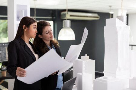 Skilled architects study printed architectural blueprints, preparing for next construction site...