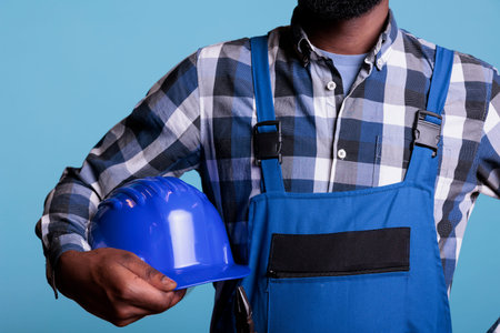 Middle section of construction worker holding protective helmet under his arm. African American man...