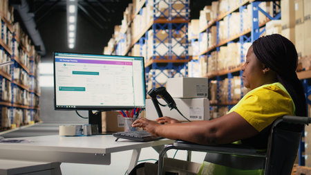 African american wheelchair user in safety vest processing cargo orders on pc at desk, logistics...