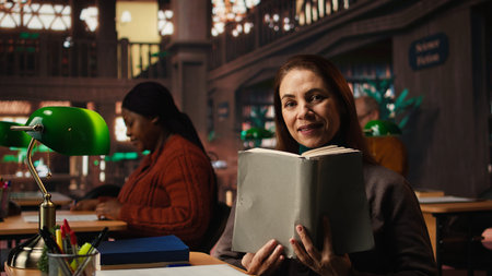 Older woman paying attention to reading hobby at the public library, enjoying storytelling for...