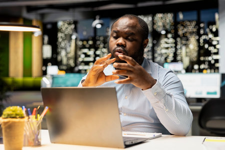 African american boss joining online meeting late in corporate office, chatting with webcam on...