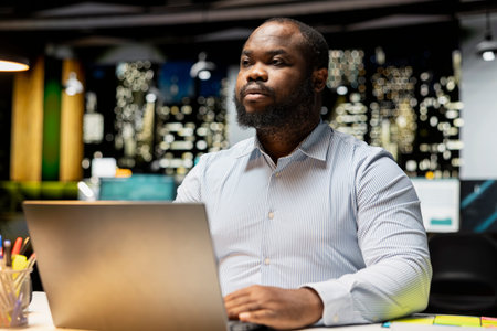 Black employee engages in methodical planning at night in corporate workspace, projecting new ideas...