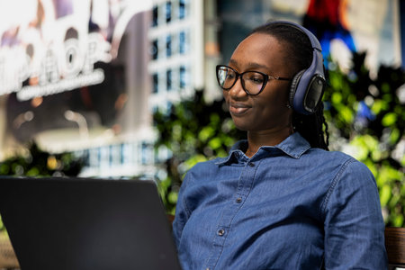 Relaxed person on park bench uses laptop to watch movies, smiling. Happy African american woman...