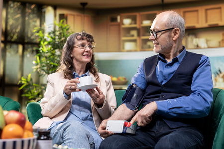 Senior husband and wife using blood pressure monitor as part of in-home healthcare. BP monitor...