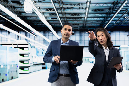Team of business professionals in microchip factory cleanroom overseeing hardware production...