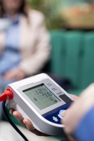 Close up of senior man pressing button on blood pressure device, measuring the pulse and vital signs for in-home daily routine. Medical BP monitor ensures disease prevention and wellness.の写真素材