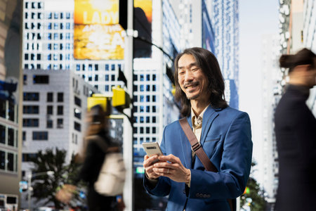 Portrait of asian business professional checking his phone and walking through the city, crowd of...
