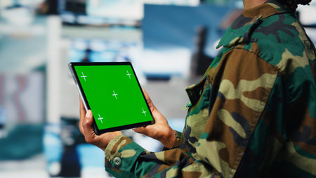 Military operator in war room oversees mission operations using green screen tablet. African american army soldier using chroma key device to do surveillance and threat monitoring, camera Bの写真素材