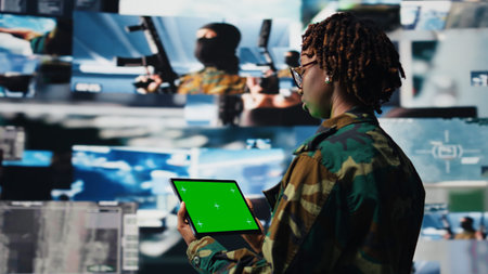 Military operator in war room oversees mission operations using green screen tablet. African...