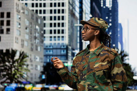 Army soldier patrolling on city street sidewalk, tasked with town security. African american female military officer in camouflage uniform strolling on metropolitan area boulevard, defense concept