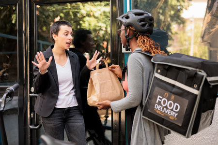 Unsatisfied client refuse taking wrong food order from delivery service courier, angry customer. Woman giving impulsive furious employee takeaway meal near company building