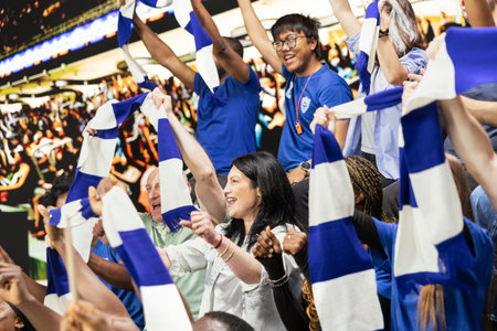 Singing blue team football fans waving scarves and cheering together in packed stadium stands during energetic live soccer match. Team spirit and celebration inside the packed stadium.