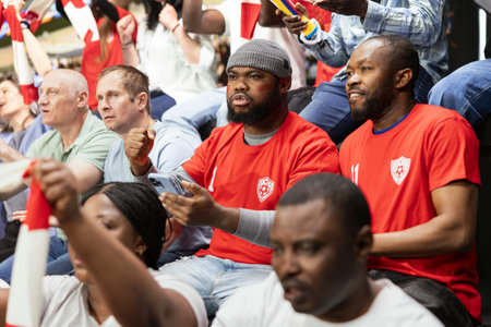 Black soccer fans using mobile sportsbook app during live football match, monitoring live odds and predictions on phone. Crowd of cheering fans, excitement and tension of in-play betting.