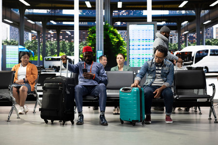 African American solo traveler in bus terminal surrounded by passengers, having trolley bag and backpack. Man checks departure time information on screen before boarding interstate bus.