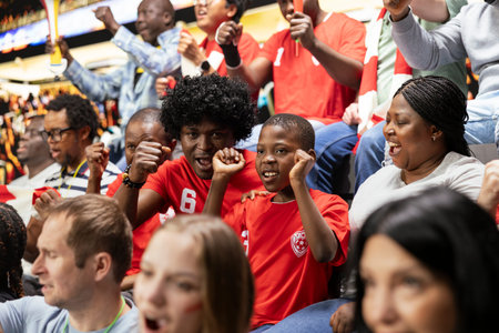 Black family cheering together at football stadium during exciting match for home team. Parents supporting their child fan while enjoying family bonding and unforgettable shared experience.