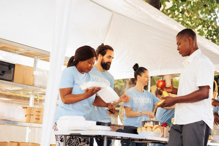 Diverse group united by charity, assisting the needy, donating food and offering support to homeless people. Volunteers supporting hunger relief initiative, providing free warm meals to the poor.