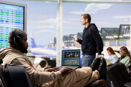Black videographer reviewing film montage and editing in post production, seated in airport lounge before boarding. International travel with nomadic lifestyle, work anywhere concept.