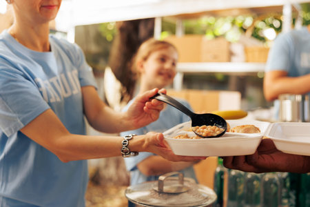 Close-up shot of caucasian charity worker providing fresh warm meal from an outdoor food bank to a person in need. Detailed view of free food being provided to the hungry and less fortunate.