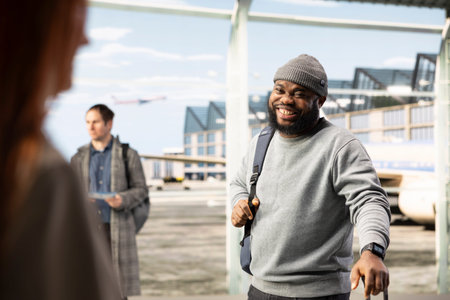 Smiling man carrying luggage and backpack in airport terminal excited to hop on plane and start vacation. Cheerful African american traveler waiting for airplane, delighted by holiday trip