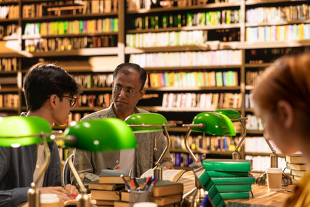 Mentor and student discussing research over open books at wooden library table, study group and collaborative learning. Academic study session framed by green lamps and stacked books.